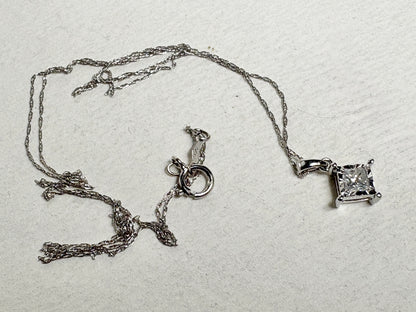 A 10k white gold pendant necklace with a princess cut diamond on a thin rope chain.