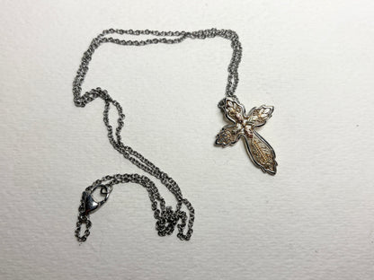 A Black Hills Gold ornate cross pendant with a sterling silver frame on a stainless steel chain.