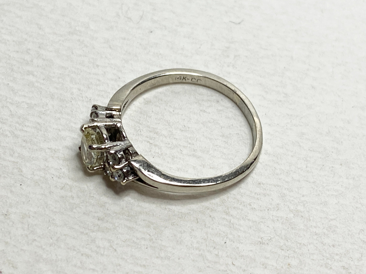 A 14k gold ring with a light yellow center diamond and white side diamonds.