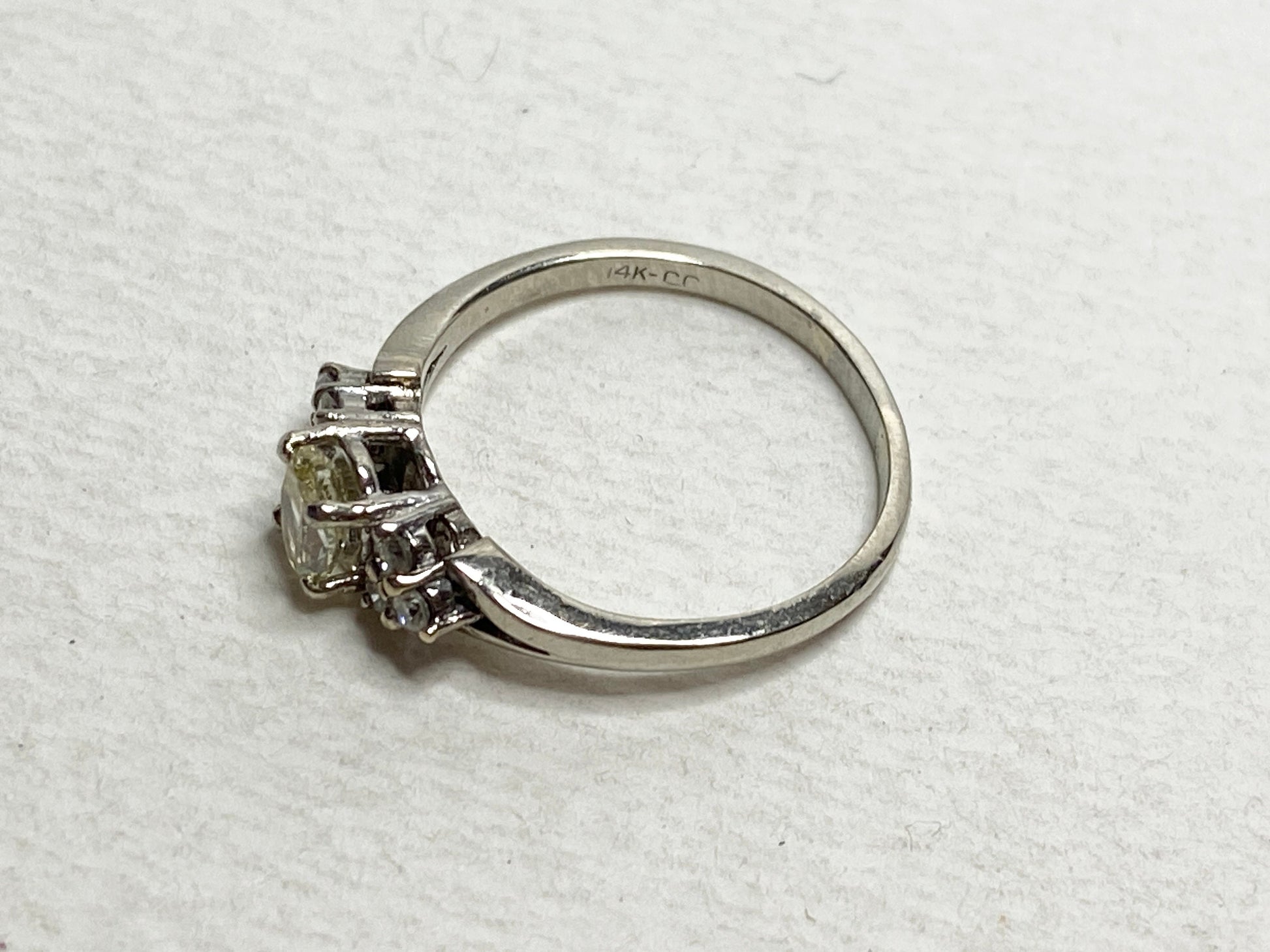 A 14k gold ring with a light yellow center diamond and white side diamonds.