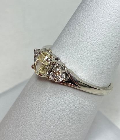 A 14k gold ring with a light yellow oval diamond and white side diamonds.