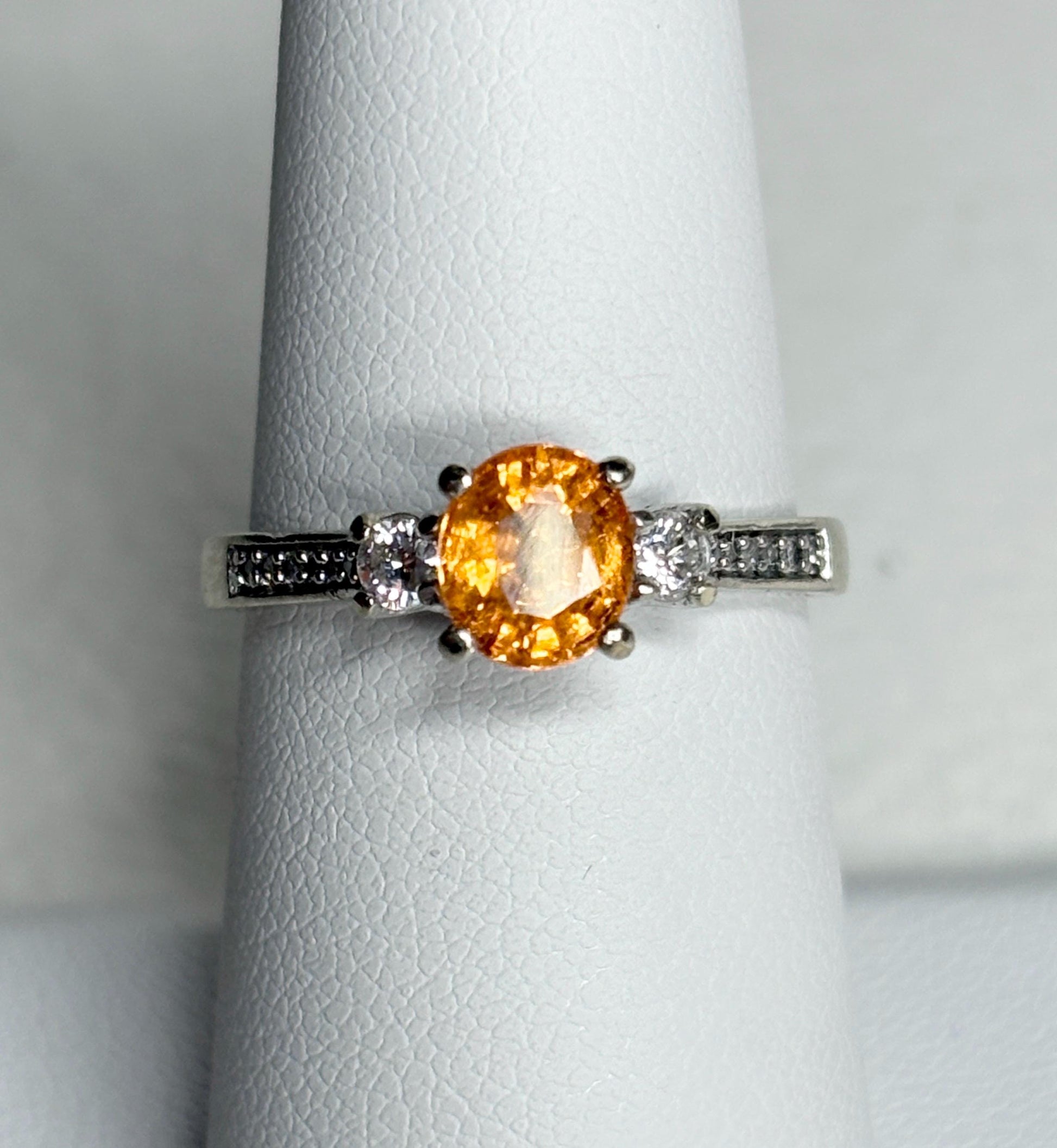 A 10k white gold ring with a central orange spessartite garnet and accent diamonds.