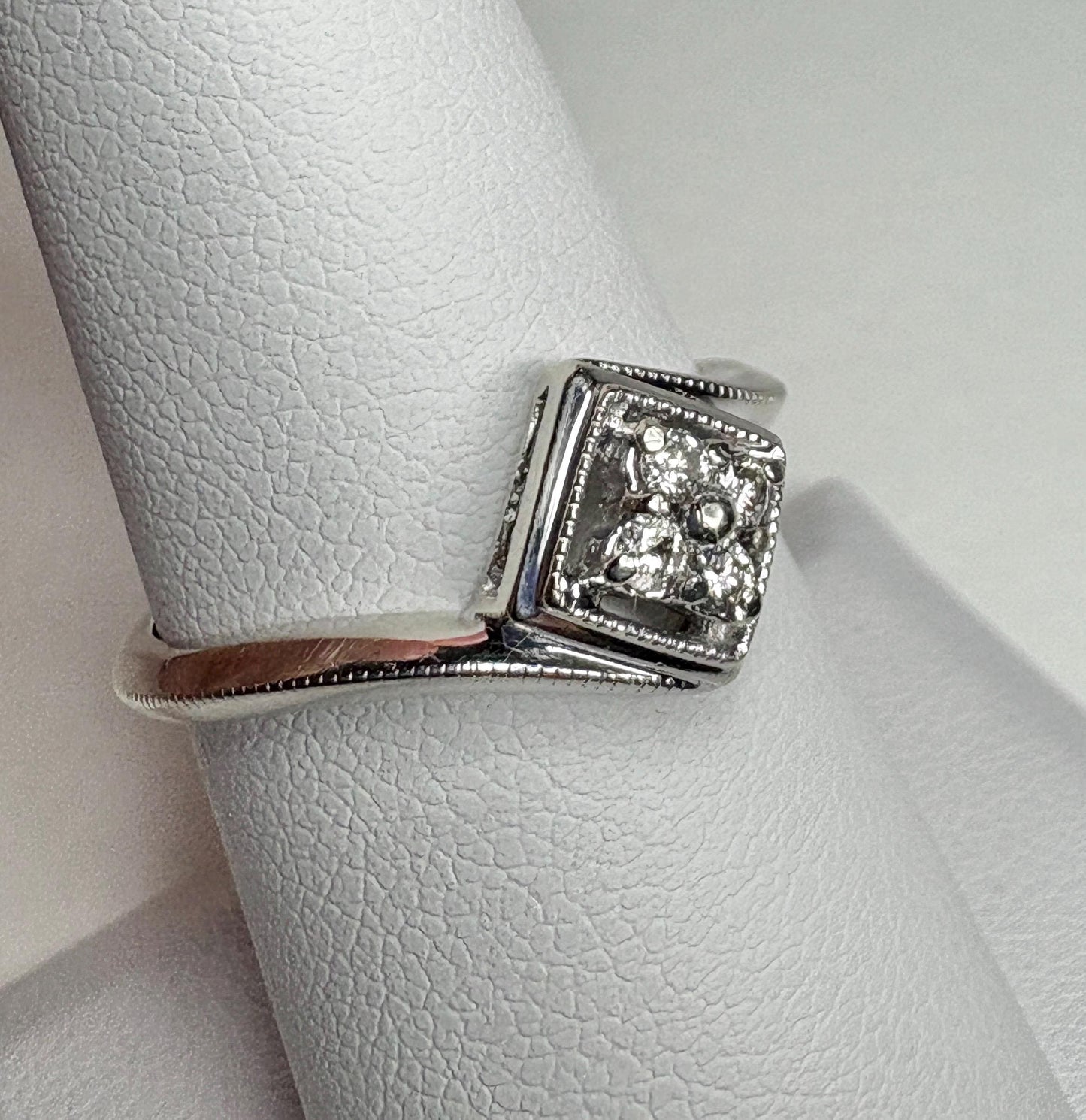 A white gold ring with a square diamond cluster and milgrain detailing.