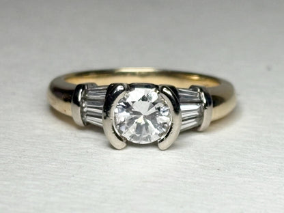 A 14k two-tone gold ring with a round diamond and baguette side stones.
