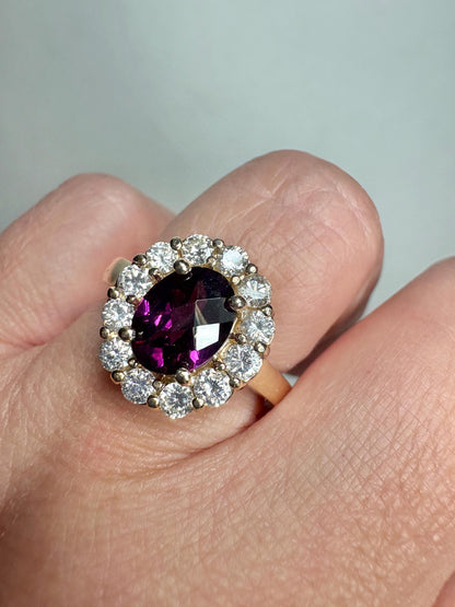 Oval checkerboard faceted rhodolite garnet ring surrounded by diamonds in a yellow gold halo setting.